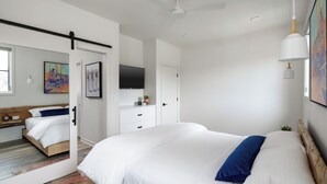 A modern bedroom with a large bed, a ceiling fan, a mounted TV, and artwork on the walls. - Elevated, Boutique Space on the Swamp Rabbit Trail (Travelers Rest)