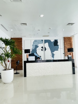 A modern reception area with a large abstract wall art, a reception desk, and a potted plant. - Abreeza place tower 2 (Davao City)