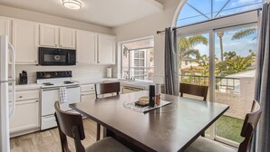 A modern kitchen with white cabinets, a black microwave, and a stove. There is a dining area with a table and chairs, and a large window offering a view of palm trees and a building. - 1 Block to Pacific Beach/FOOD/Bars, Updated, 2-Car Garage w/fee, Yard, Sleeps 14 (San Diego)