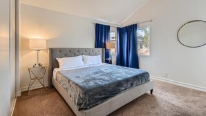A bedroom with a bed, a bedside lamp, a round mirror, and a window with curtains. - 1 Block to Pacific Beach/FOOD/Bars, Updated, 2-Car Garage w/fee, Yard, Sleeps 14 (San Diego)