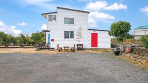 A two-story white building with a red door, a blue door, and a small porch with wooden furniture. - Jeju Orsirok Dogchaepension (Jeju City)