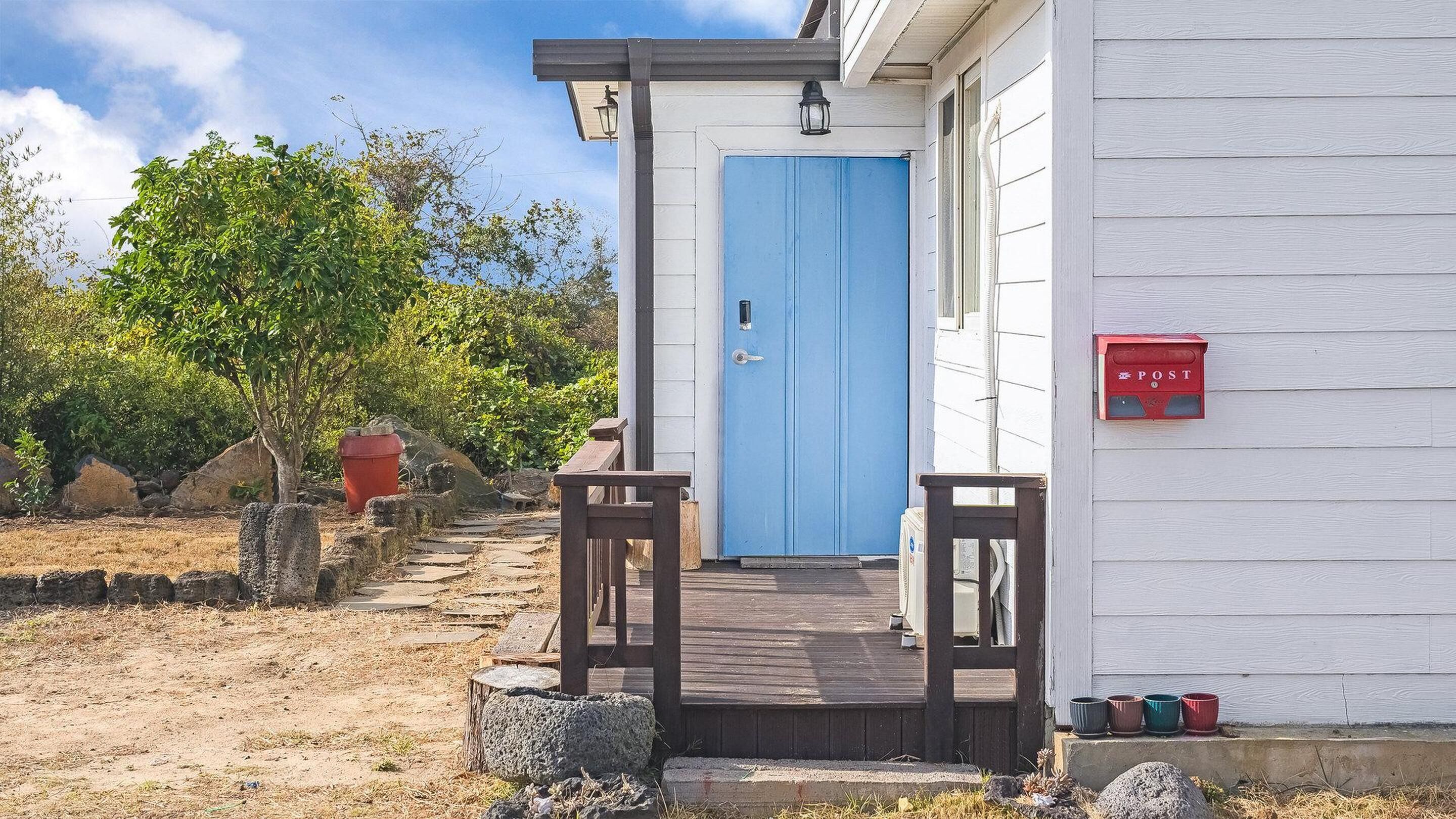 Ein Haus mit blauer Tür, einer Holzveranda und einem roten Briefkasten.