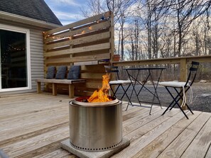 A deck with a metal fire pit, wooden benches, and a table with chairs. - The Under Ridge Home - 4 Bedroom w/Fireplace (Gardiner)