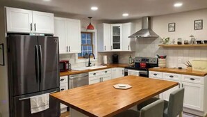 Una cucina moderna con mobili bianchi, un frigorifero in acciaio inox, un'isola in legno e una lampada a sospensione rossa.