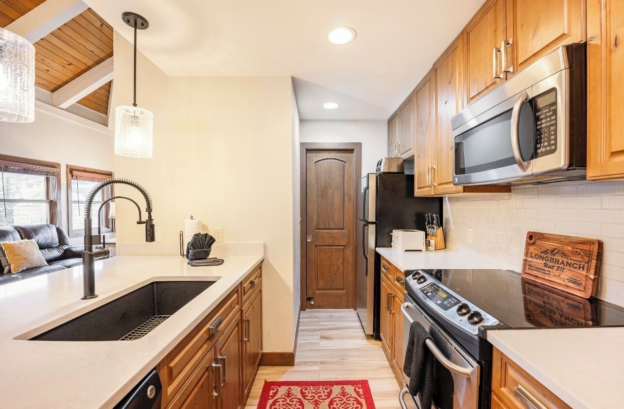 A kitchen with wooden cabinets, a stainless steel microwave, a stove, and a sink.