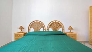 A bed with a green bedspread, two nightstands with lamps, and a wicker headboard. - Appartamento Claudio by Barbarhouse (Ugento)
