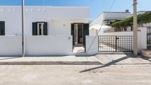 A modern white building with a gated entrance, a small porch, and a visible air conditioning unit. - Appartamento Claudio by Barbarhouse (Ugento)