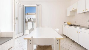 A bright, modern kitchen with white cabinetry and a large dining table. - Appartamento Claudio by Barbarhouse (Ugento)