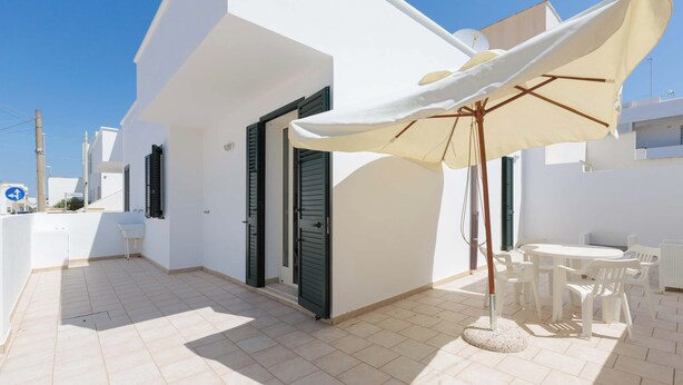 A white building with a tiled patio, a white table with chairs, and a beige umbrella. - Appartamento Claudio by Barbarhouse (Ugento)