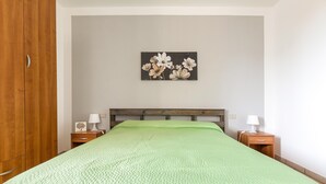 A bedroom with a green quilted bedspread, a wooden headboard, two bedside tables with lamps, and a floral artwork on the wall. - 2468 Casa Sofia by Barbarhouse (Ugento)
