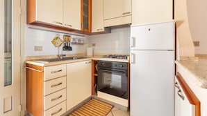 A compact kitchen with wooden cabinets, a gas stove, a built-in oven, and a white refrigerator. - 2468 Casa Sofia by Barbarhouse (Ugento)