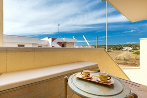 Un balcón con un banco acolchado y una mesa con dos tazas y platillos.