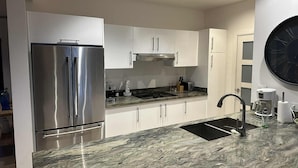 Una cocina moderna con armarios blancos, un refrigerador de acero inoxidable, un lavamanos negro y una encimera de mármol.