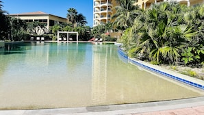 Una piscina con agua azul cristalina, rodeada de palmeras y un edificio con varios balcones.