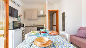 A compact kitchen with a microwave, stove, and cabinets. There is a dining table with a colorful tablecloth and various dishes. - 2369 Mono Le Rose by Barbarhouse (Ugento)