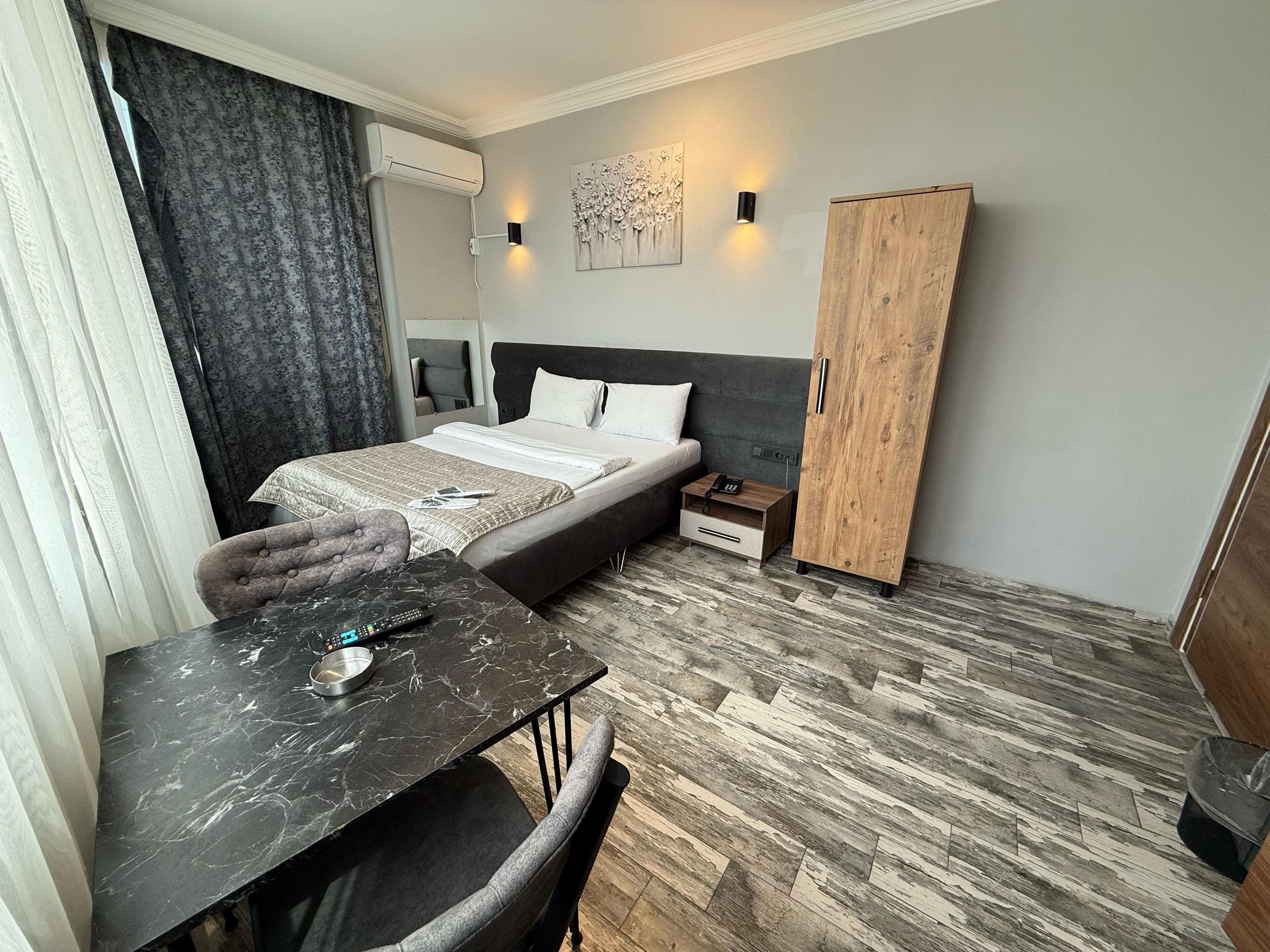 A hotel room with a bed, bedside table, chair, wardrobe, and a small table with a remote control.
