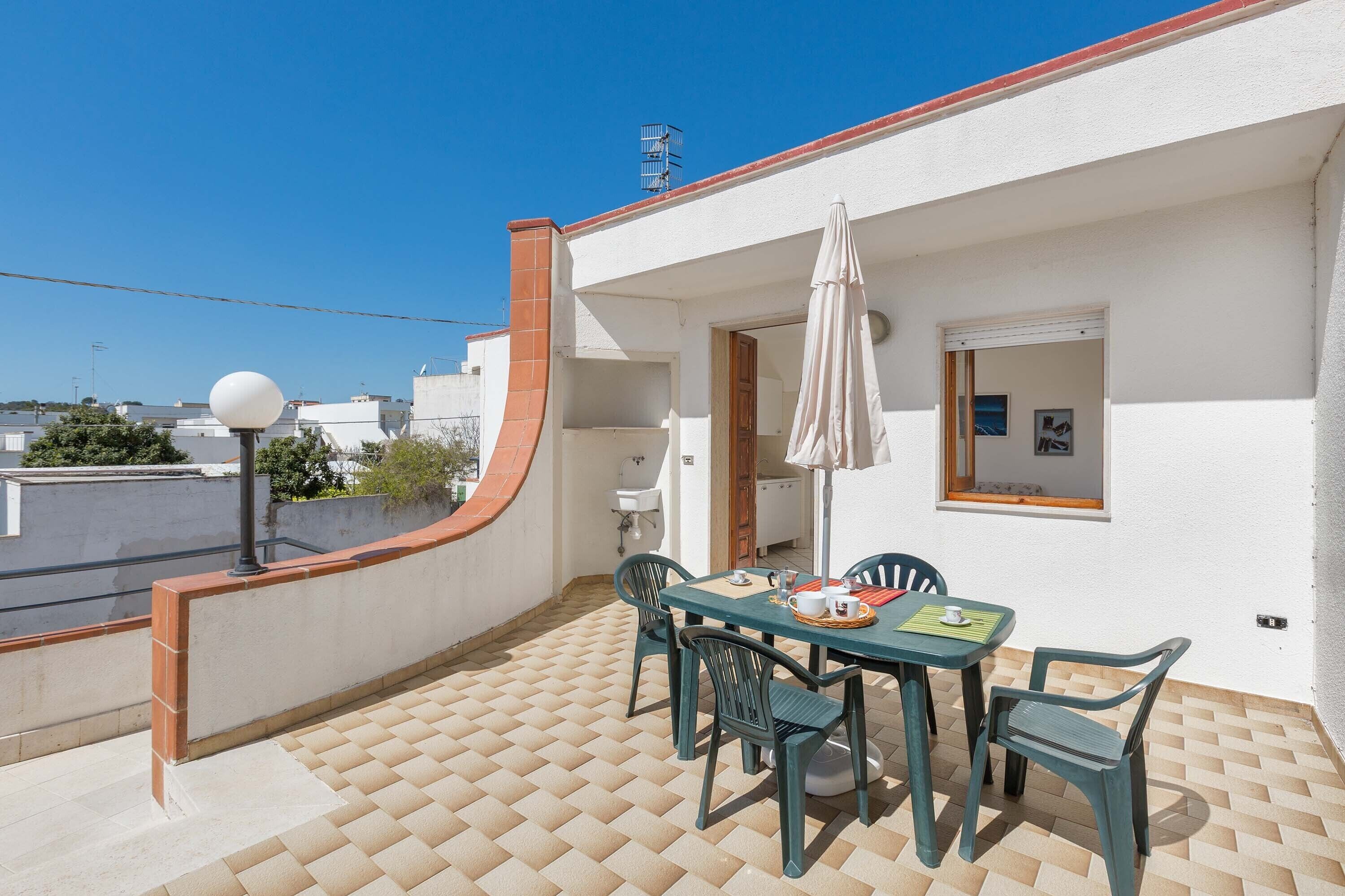 A balcony with a tiled floor, a table with chairs, a white umbrella, and a view of the city.