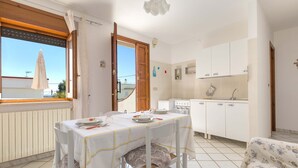 A dining area with a table set for two, a kitchen with white cabinets, and a view through an open door. - 2810 Case al Tacco - Appartamento Mare by Barbarhouse (Castrignano del Capo)