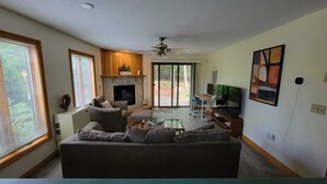 Un salon avec une cheminée, un canapé, un téléviseur et un ventilateur de plafond.