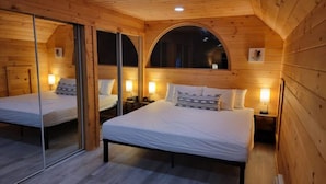 Une chambre dans un chalet en bois, avec deux lits, chacun muni d’une table de chevet et d’une lampe.