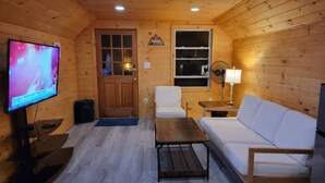 Un intérieur de chalet chaleureux, avec un revêtement mural en bois, un téléviseur, un canapé, une table et un ventilateur.
