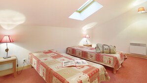 A bedroom with two beds, a skylight, bedside lamps, a bedside table, and a wall-mounted heater.