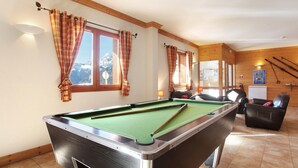 A pool table in a room with wooden walls and a view of mountains through the windows.