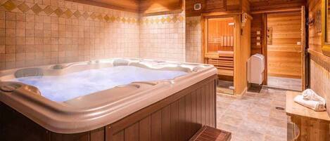 A wooden interior with a hot tub, wooden benches, and a tiled wall.