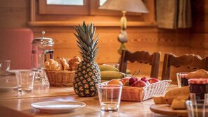 Una mesa de comedor de madera con una piña como centro, varias frutas, pan y condimentos.