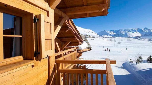 Una cabaña de madera con balcón con vistas a un paisaje montañoso nevado.
