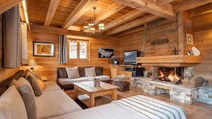 Acogedor interior de cabaña de troncos con chimenea de piedra, mobiliario de madera y televisor.