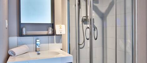 Ein modernes Badezimmer mit einer in Glas eingefassten Dusche, einem Waschtisch mit Spiegel und einem Handtuch auf der Ablagefläche.