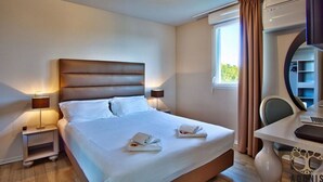 Ein Hotelzimmer mit einem großen Bett, Nachttischlampen, einem Schreibtisch und einem Fenster mit Vorhängen.