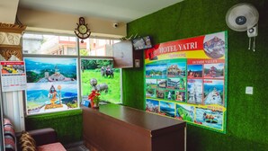 Zona de recepción de un hotel, con mostrador, calendario en la pared, reloj, ventilador de pared y un cartel grande que anuncia recorridos turísticos.