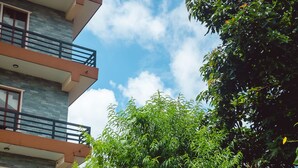 Una camioneta blanca estacionada frente a un edificio con balcón y un árbol de hojas verdes.
