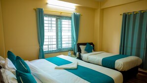 Habitación de hotel con dos camas, ropa de cama color verde azulado, una ventana con cortinas y suelo de madera.
