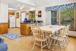 A kitchen with a refrigerator, wooden cabinets, a dining table with chairs, a window with a view, and a ceiling fan. - A Peace of Quiet | 1,025 ft. to the Beach | Private Pool (Duck)