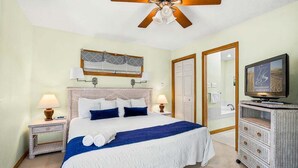 A hotel room with a bed, two bedside lamps, a ceiling fan, a television, and a bathroom visible through an open door. - A Peace of Quiet | 1,025 ft. to the Beach | Private Pool (Duck)