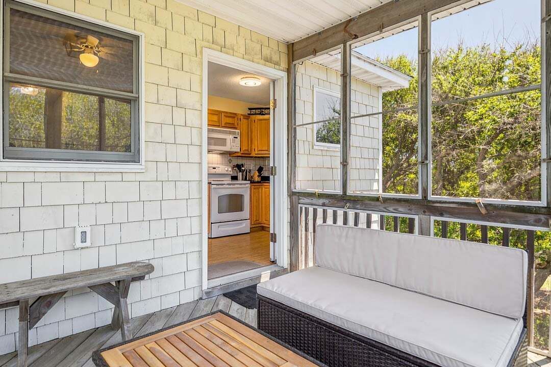 A covered porch with a bench, a wooden table, and a view into a kitchen area.