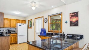 A kitchen with wooden cabinets, a white refrigerator, a microwave, and a large window. - A Peace of Quiet | 1,025 ft. to the Beach | Private Pool (Duck)
