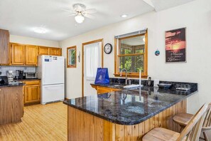 A kitchen with wooden cabinets, a white refrigerator, a microwave, and a large window. - A Peace of Quiet | 1,025 ft. to the Beach | Private Pool (Duck)