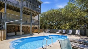 A swimming pool with a wooden deck, lounge chairs, and a multi-story building with balconies. - A Peace of Quiet | 1,025 ft. to the Beach | Private Pool (Duck)