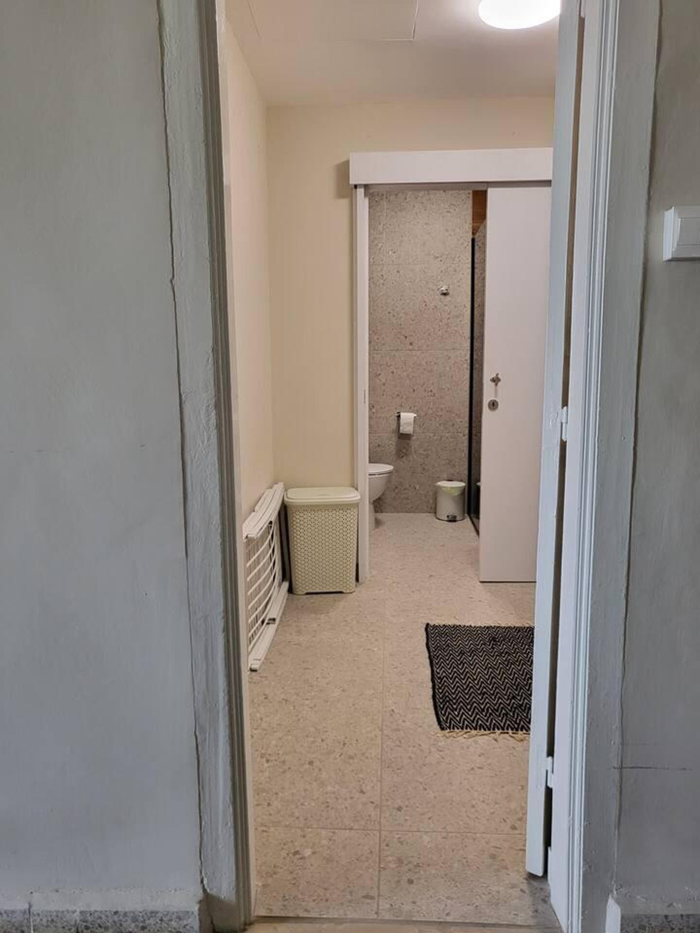 Ein schmaler Flur, der zu einem Badezimmer mit Toilette, einem kleinen Mülleimer und einem Heizkörper führt.