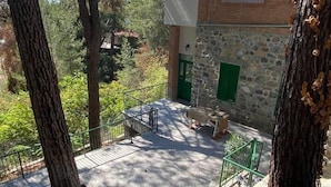 A stone building with a green door, a balcony with a metal railing, and trees in the background. - Theplatresnest Lovely 3-bed House in Pano Platres (Platres)