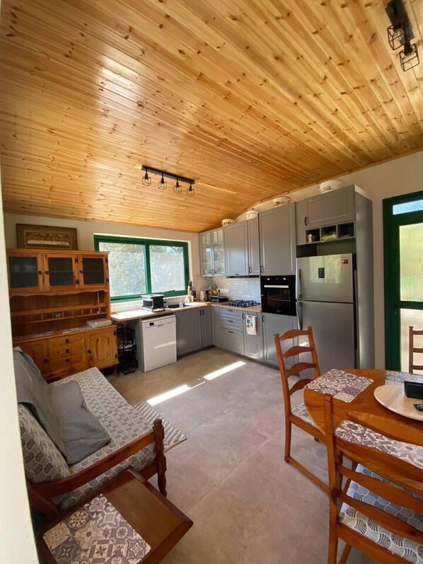 A compact kitchen with wooden cabinets, a built-in oven, and a refrigerator. There is a dining area with a table and chairs, and a sofa in the corner.