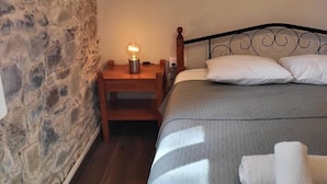 A bedroom with a stone wall, a wooden nightstand with a lamp, a bed with white pillows, and a folded towel on the bed. - Theplatresnest Lovely 3-bed House in Pano Platres (Platres)