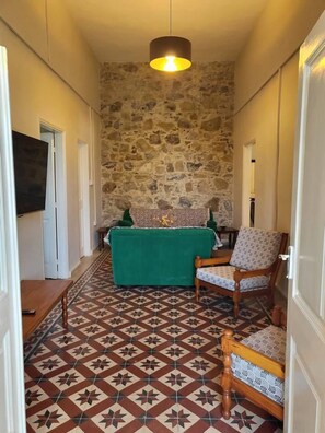A narrow hallway with a stone wall, a green sofa, two patterned armchairs, and a hanging light fixture.