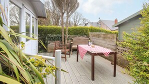 A wooden deck with a table and chairs, surrounded by greenery and a white building. - Pebble Reef (Portland)