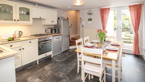 A modern kitchen with white cabinets, a built-in oven, and a microwave. There is a dining area with a table set for two, chairs, and a vase with flowers. - Pebble Reef (Portland)