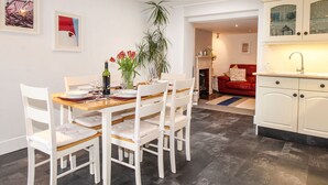 A dining area with a wooden table and white chairs, a vase with red flowers, and a bottle of wine. - Pebble Reef (Portland)